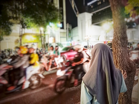 Small hijab girl  who will cross in a busy street of vehicles in Surabaya, Indonesia.
