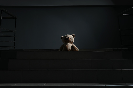 Lonely teddy bear on grey stairs indoors, low angle view