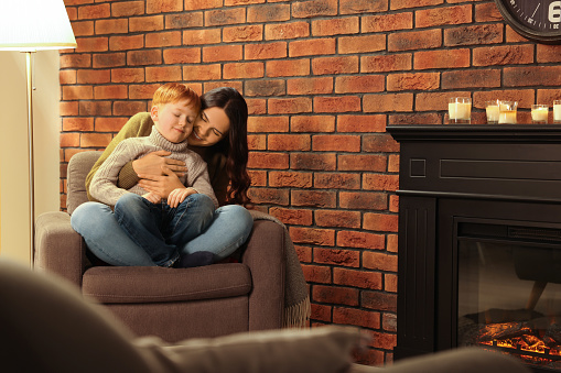 Happy mother and son hugging near fireplace at home