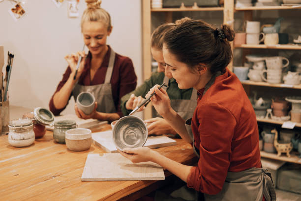 A company of three cheerful young women friends are painting ceramics in a pottery workshop. stock photo