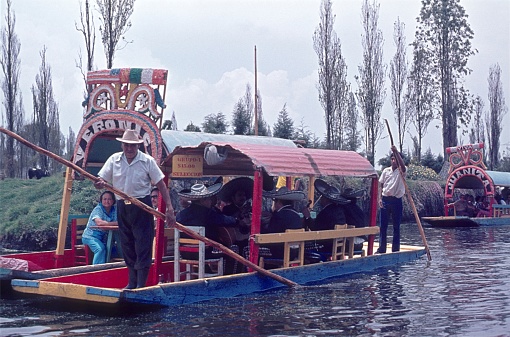 Mexico, Mexico City, 1974. Tour boats on a canal in Xochimilco Municipal Park. Furthermore: boat owners, day trippers and a mariachi band.