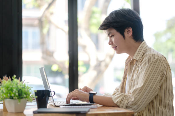 istock Side view of young start up businessman using laptop computer at desk in modern workplace. 1499597657