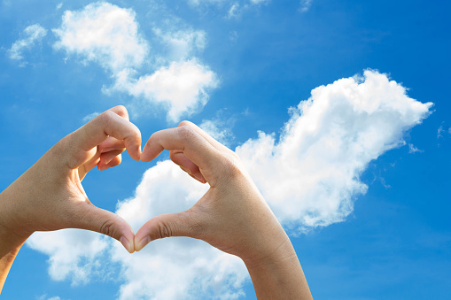 Woman hand making heart shape on bright sky