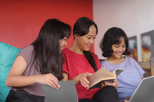 Close-up shot of Indonesian mother and her teenage girls have a reading time together at home.