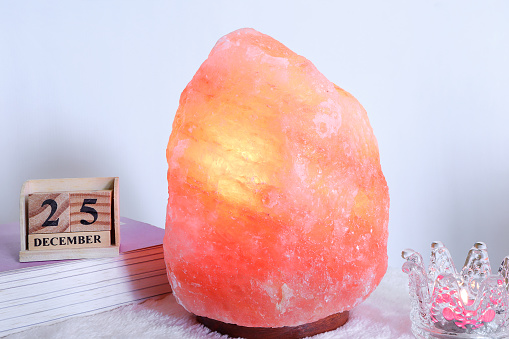 Himalayan salt lamp, Cube wooden calendar showing date on 25, December, candle and decor on tables in living room. lamp with pink salt crystals.