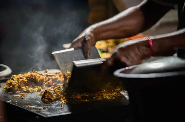 Photo of Hands of the kottu roti vendor, making kottu on top of a hot steel grill plate