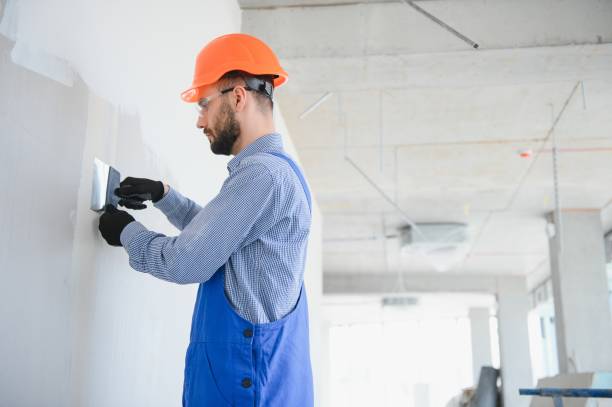 istock man drywall worker or plasterer sanding and smoothing a plasterboard walls with stucco using a sandpaper holder. Wearing white hardhat and safety glasses. Panoramic image with copy space 1499647403
