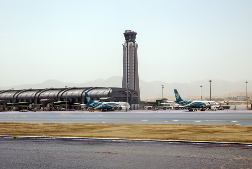 Muscat, Oman - May 22, 2023: Muscat airport control tower. Oman Air planes at the boarding gates of the airport in Muscat. Sultanate of Oman