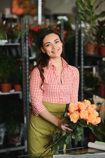 Cute girl florist collects a bouquet of roses in a flower shop. A beautiful florist creates a composition of flowers. Girl cuts flowers and removes stale leaves.