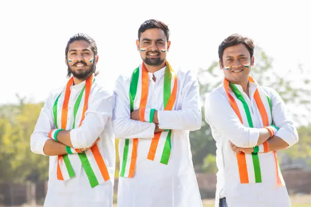 Group Portrait of young indian men wearing traditional white kurta and tricolor duppata standing cross arms at park. Election and politics, celebrating Independence day or Republic day.