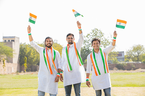 Group of happy young men wearing traditional white dress holding indian and weaving flag while standing at park celebrating Independence day or Republic day.