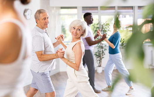 Mature man dances steamy salsa with elderly female companion for fitness classes and enjoys movement and activity. Hobbies, active pastime
