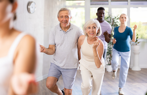 Cheerful elderly amateur couple visiting group choreography class, practicing vigorous lindy hop moves. Concept of active lifestyle