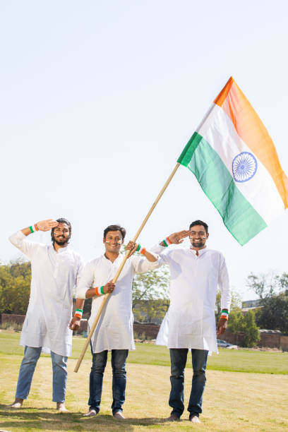 grupa szczęśliwych młodych mężczyzn w tradycyjnych białych strojach trzymających indyjską flagę i salutujących, świętujących dzień niepodległości lub dzień republiki. - child patriotism saluting flag zdjęcia i obrazy z banku zdjęć