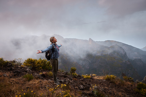 Smiling female backpacker standing on a mountain with her arms outstretched. Copy space.