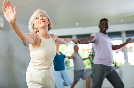 Cheerful elderly woman practicing vigorous lindy hop moves paired with african american male partner in dance class. Social dancing concept