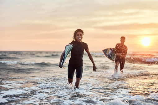 Cheerful female surfer running away from her boyfriend during summer sunset through sea. Copy space.