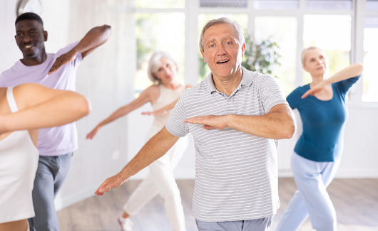 Enthusiastic elderly man practicing modern vigorous dance movements in group dance class with mature people