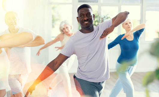 Portrait of cheerful adult african american man enjoying active dancing during group training in dance studio