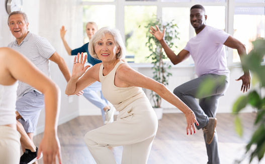 Cheerful elderly woman attending group choreography class, learning modern dynamic dances. Concept of active lifestyle of older generation