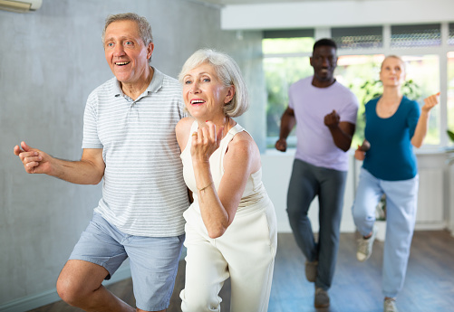 Positive aged man and woman dancing energetic upbeat jive as couple during group training in dance studio