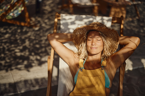 Young smiling woman relaxing on a deck chair with her eyes closed on the beach.