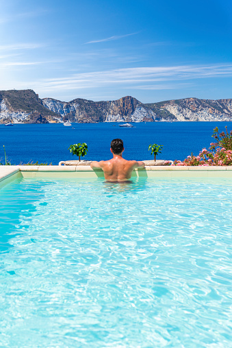 Rear view of a cool man relaxing at the edge of the swimming pool by the ocean, Ponza island, Pontine Islands, Latium, Italy, Europe