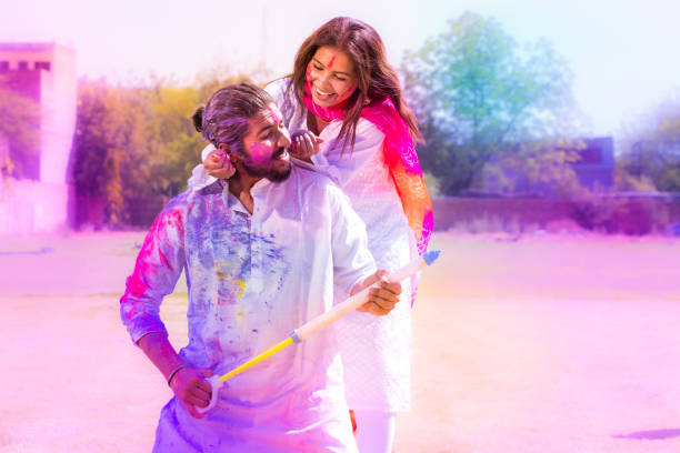 cheerful young indian couple playing with colorful powder color or gulal celebrating holi festival at park outdoor. - kurta imagens e fotografias de stock