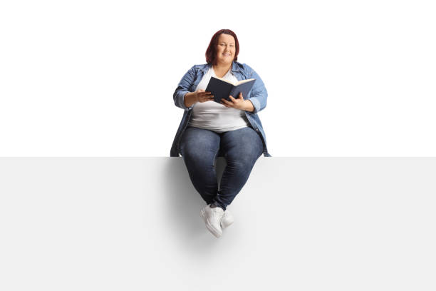 istock Young corpulent woman sitting on a blank panel and holding a book 1499669848