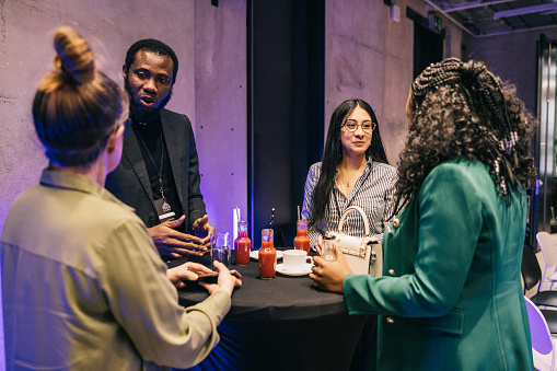 In a bustling networking area, people from different races and backgrounds enthusiastically share their experiences and expertise, creating a dynamic post-conference environment.