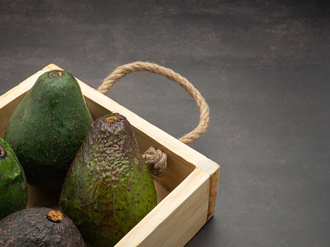 Avocados are in a wooden crate on a table. Space for text. Close-up photo. Concept of healthy fruits.