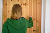 A woman standing in front of a large wooden door, knocking on the door