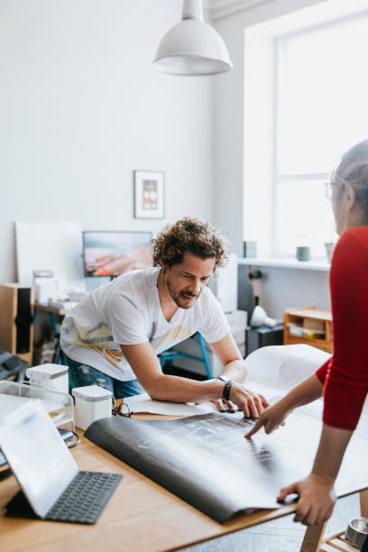 Two latin architects working with blueprints in their open space studio stock photo