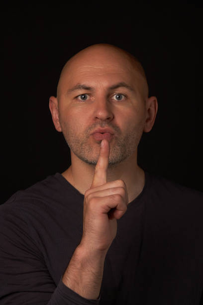 istock Bald, bearded man looks into the camera and blows on the index finger 1499677578