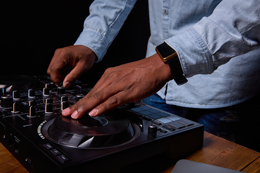 Professional dj console close up. Strong male hands of a dark-skinned man play music. The face is not visible. Smart watch on hand
