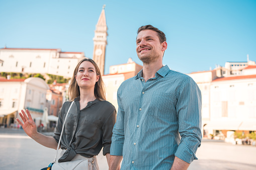 In the midst of their blissful and rejuvenating holiday, a charming mid-adult Caucasian couple enjoys a peaceful walk by the seaside, engaging in conversation, strengthening their bond, and having a great time.