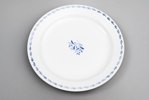 A closeup of a vintage white plate with blue floral ornaments on a gray surface