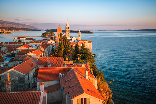 Beautiful high angle view on old insular town Rab in Croatia with church towers and house rooftops, seascape and horizon at sunset