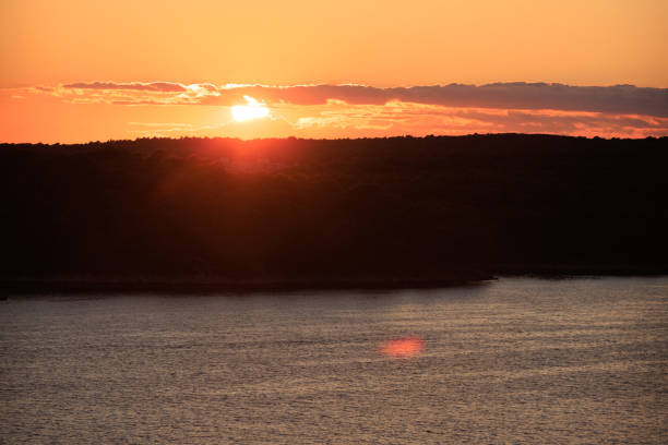 Beautiful orange colored sun between the clouds setting on horizon, view over the calm sea on Rab island in Croatia