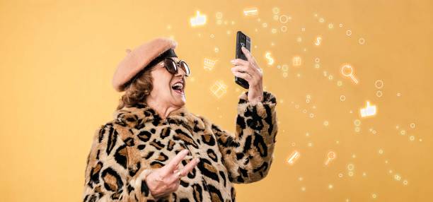 Cheerful aged woman in fashion clothes using smartphone and take a selfie stock photo