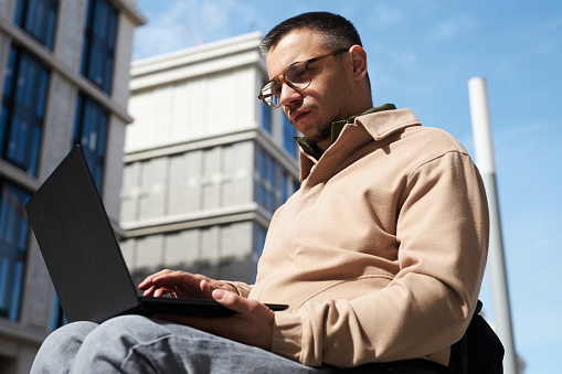 Low angle view of young man with disability concentrating on his online work on laptop outdoors