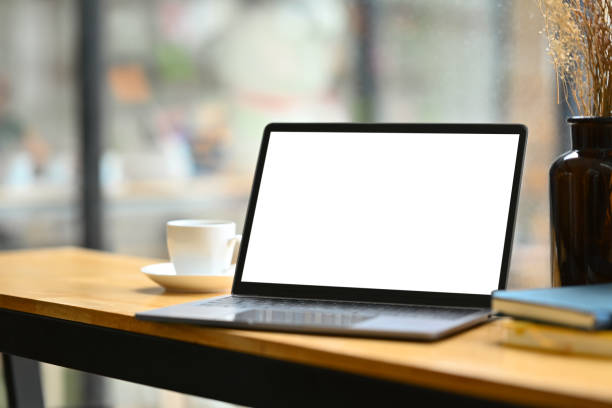 istock Wooden office desk with laptop computer, notepad, and cup of coffee. White blank screen for your advertising text. 1499689911