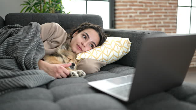 Young hispanic woman with dog smiling confident watching movie lying on sofa at home