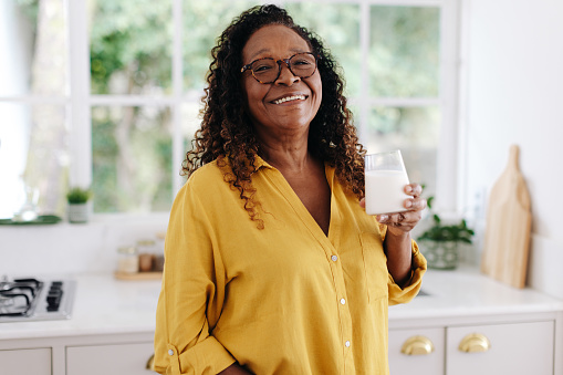 Aging black woman drinking a glass of fresh milk for breakfast, knowing that it's an important part of a balanced diet. Happy senior woman taking care of her health with her dairy product.
