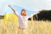 beautiful Ukrainian girl carries fluttering blue and yellow flag of Ukraine against  sky and field background. Ukrainian flag is a symbol of independence. Celebrate Constitution Independence flag day