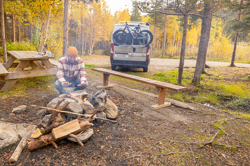 He makes a camp fire in nature, his van parked behind, the real camping lifestyle. Solitude in nature