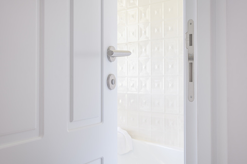White bathroom door left ajar, slightly open doorway with modern handle, selective focus