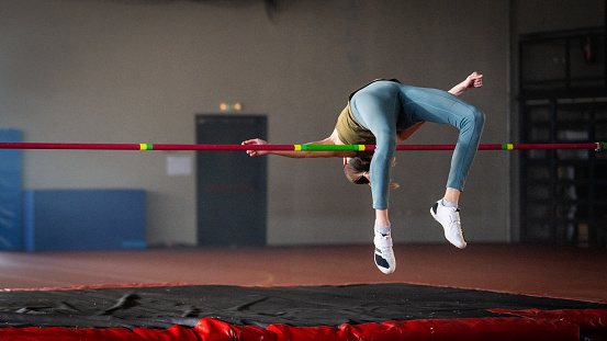Athlete young woman doing high jump in sports hall during practice.