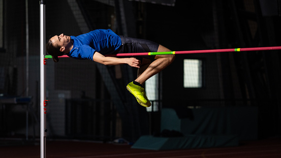 Athlete young man doing high jump in sports hall during practice.