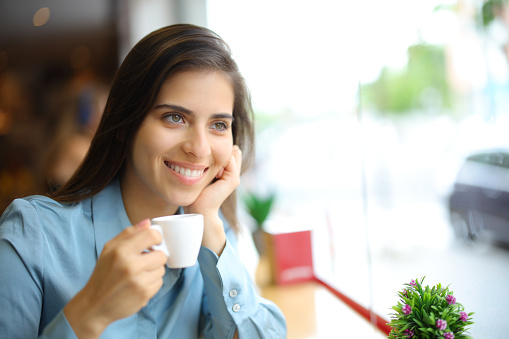 Happy woman drinking coffee in a bar looking away